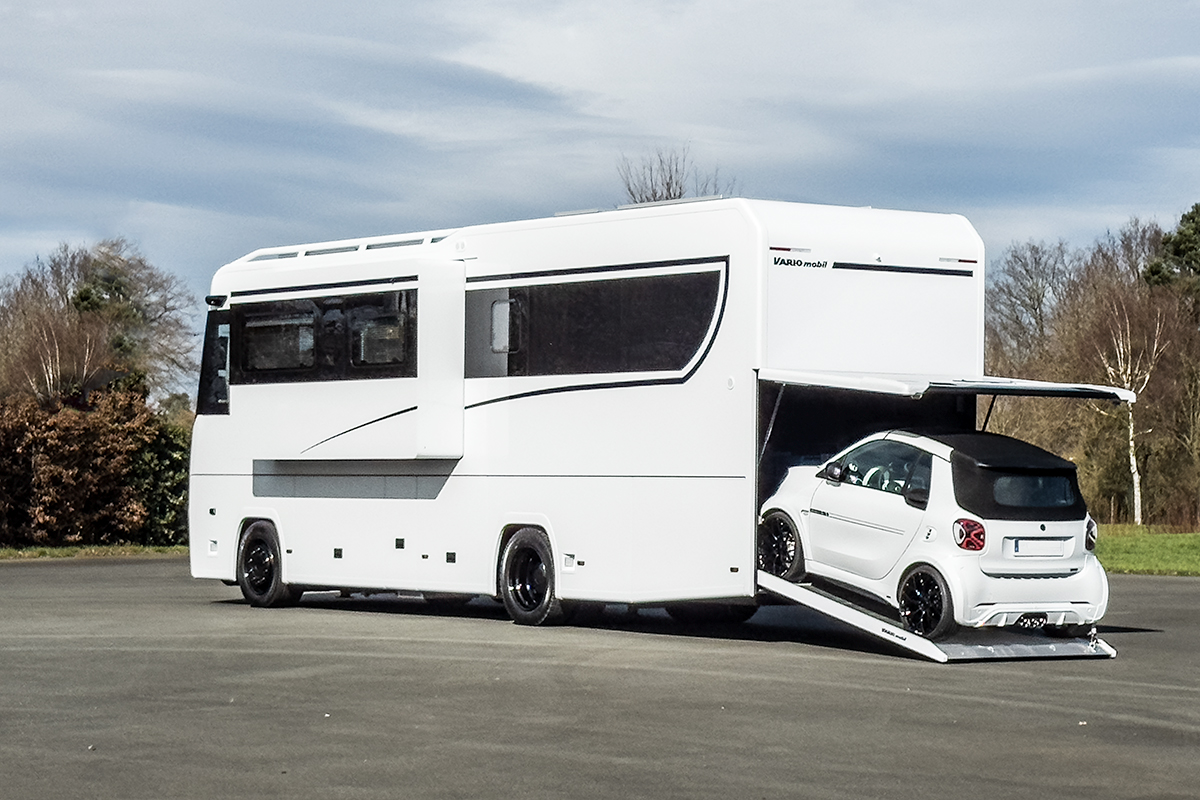 Foto des Komfort-Reisemobils VARIO Perfect 1000 auf MB Actros, hochglanz Wdeiß und Blackline Edition mit schwarzem Gals-Fensterband, schwarzen Felgen und Brabus-SMART Cabrio in der PKW-Garage