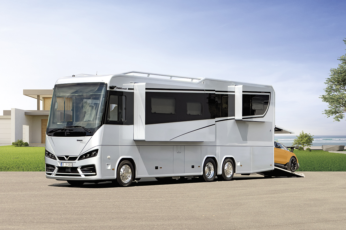 VARIOmobil VARIO Perfect 1200, silber lackiert, schwarzes Glasband, 3-Achser 26t, 12m vor modernem Haus am Meer mit orangem Roadster.