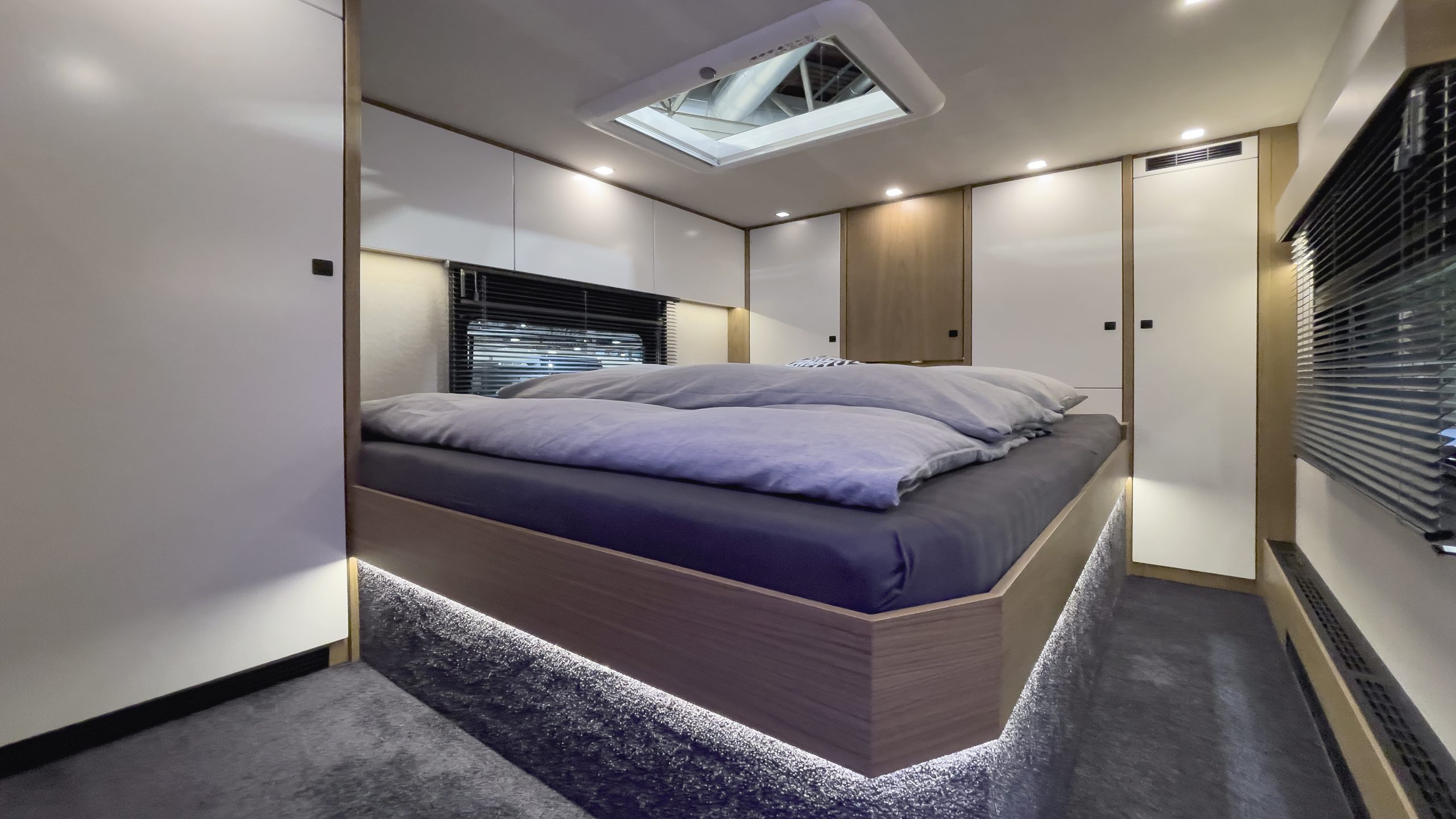 Schlafraum im VARIO Perfect 1080 in bentART Design, Edelholz Nussbaum hell gebleicht, Schleiflack-Türen in Weiß, großer Dachhaube und gegenüberliegenden Fenstern.