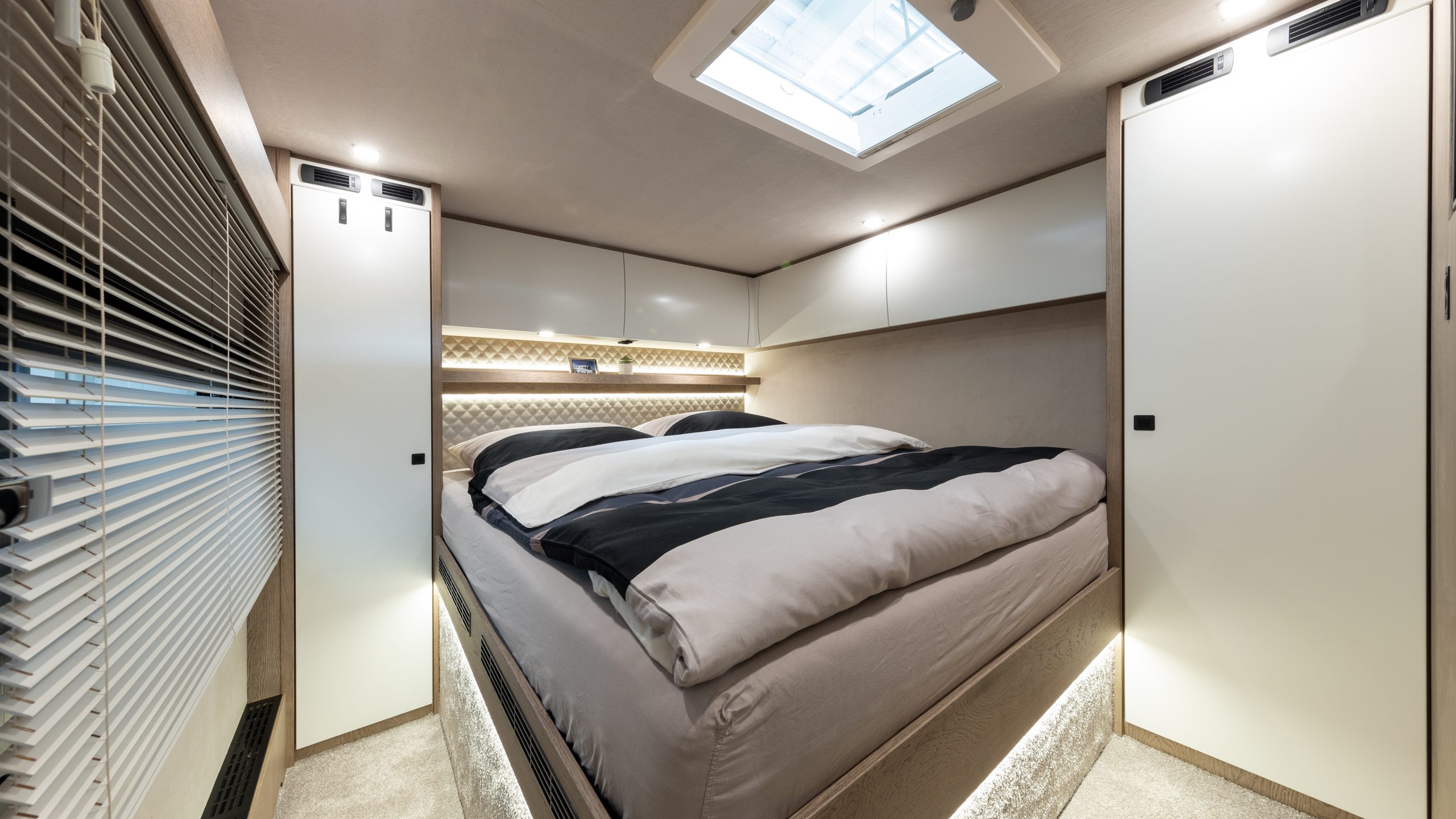 Schlafbereich im Reisemobil mit Dometic-Dachhaube (500 × 700 mm, elektrisch), Möbelfronten in Eiche silver mit bentART-Akzenten, McCoy Modern Frost black Griffen, TANDRA 11 Rautenoptik und LED-Beleuchtung am Heckbett